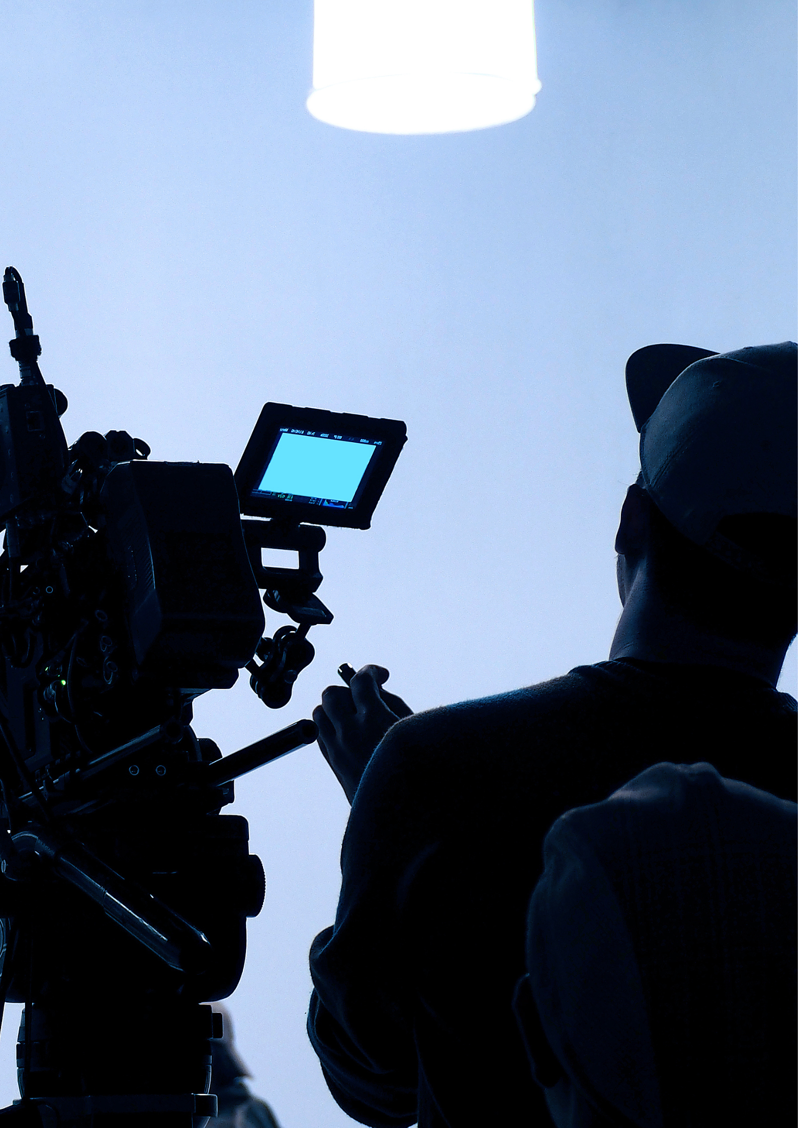 Man from behind filming in a studio with white light and large film camera sat next to him