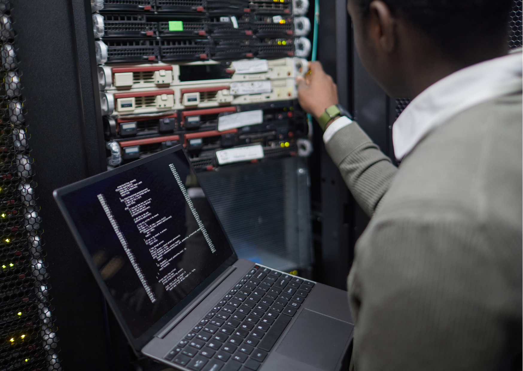 back of man wearing suit looking at large computer unit holding a laptop
